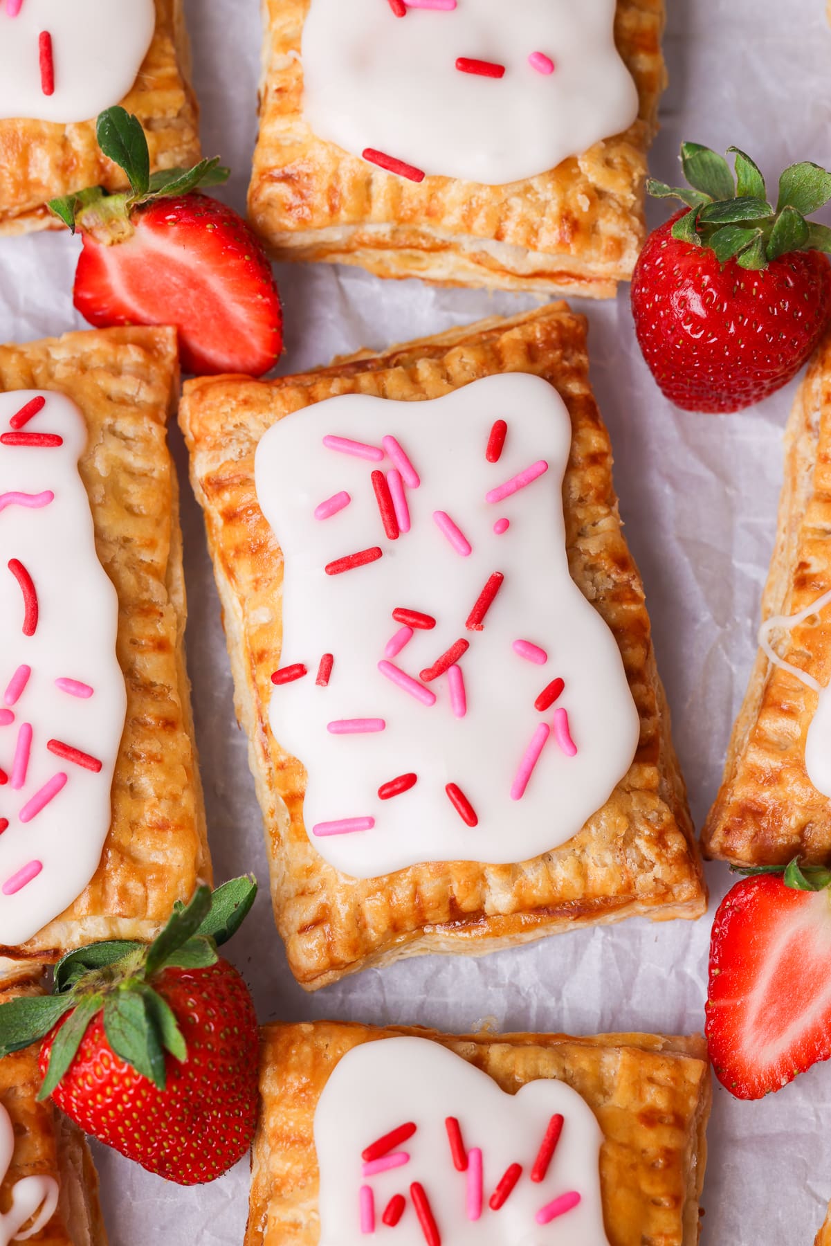 freshly baked pop tarts on parchment paper. There are strawberries around the pop tarts.